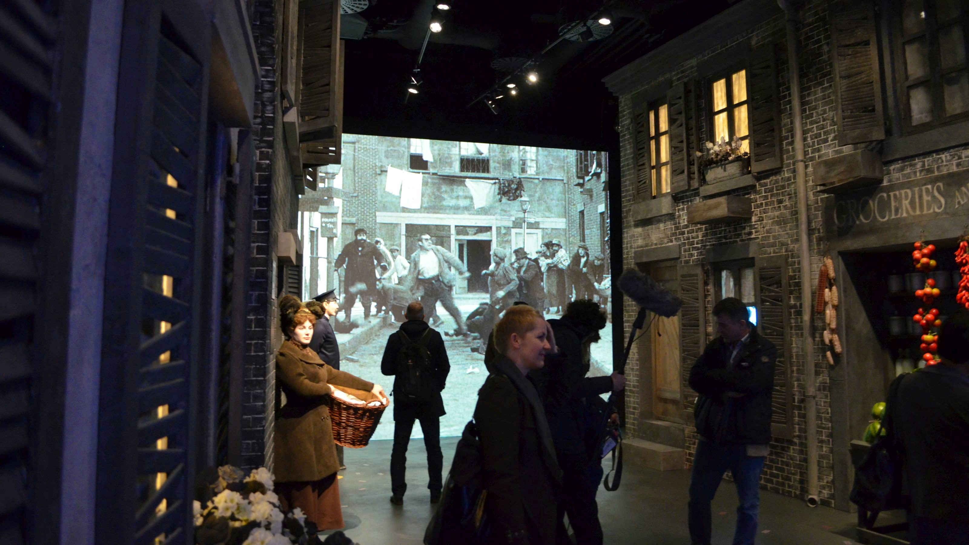Besucher laufen durch nachgestellte Filmsets, während im Hintergrund ein Stummfilm auf einer Leinwand läuft.