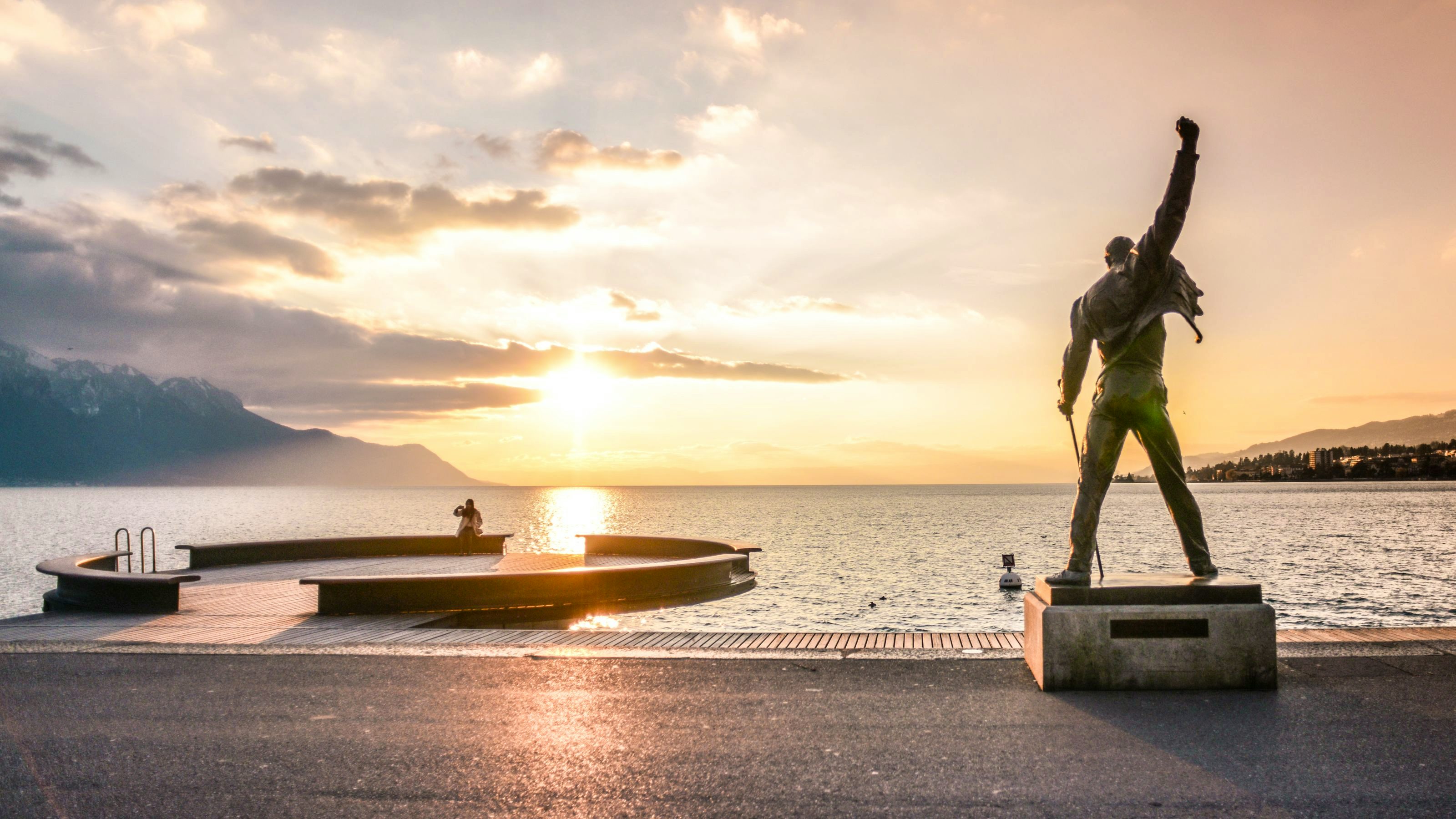 Rückansicht der Freddie-Mercury-Statue am See während eines Sonnenuntergangs.