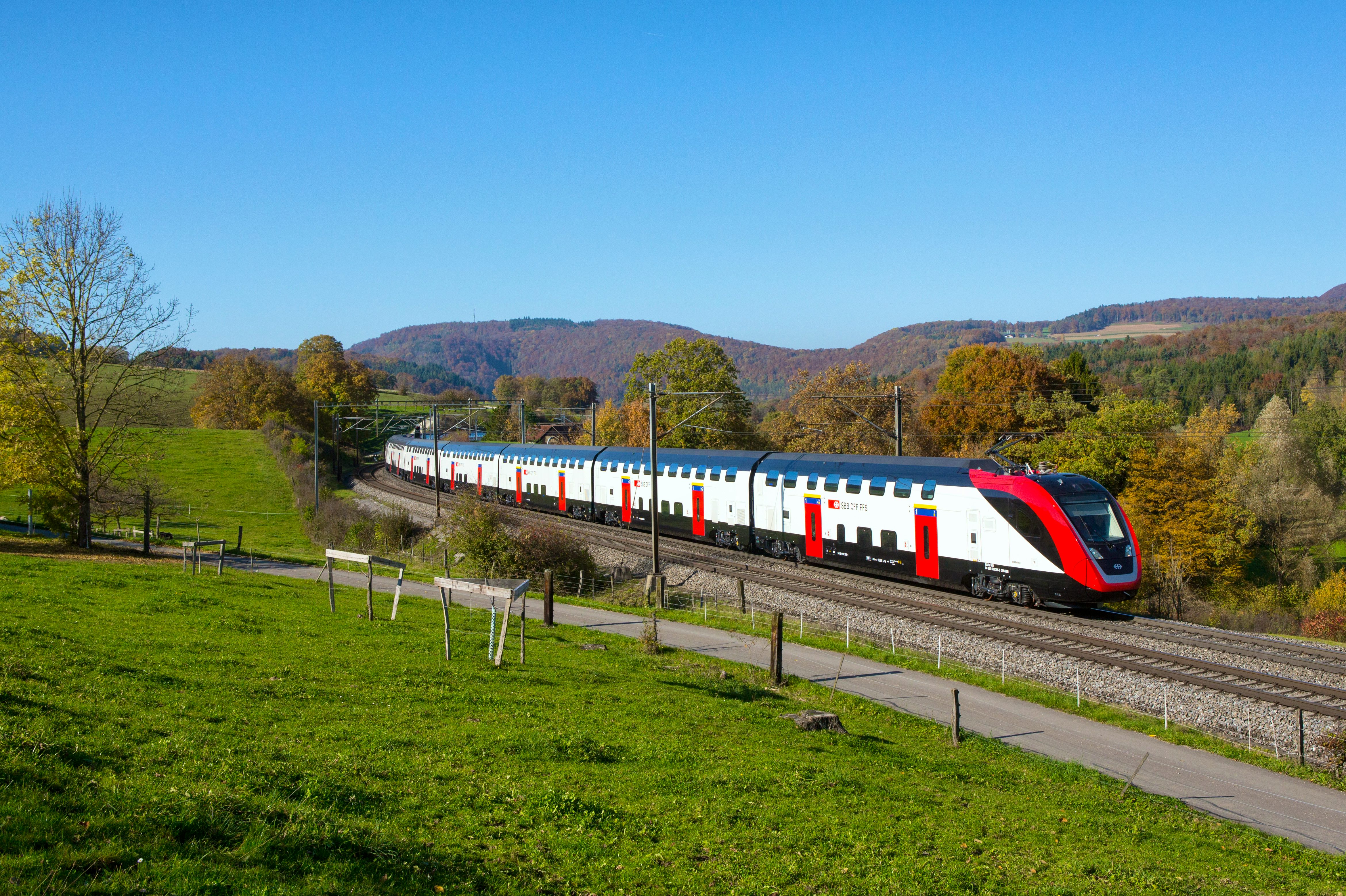 Il bipiano TLP circola in una giornata soleggiata a Zeihen, sulla tratta del Bözberg tra Basilea e Brugg. A sinistra del treno si possono ammirare un campo e una passeggiata, mentre a destra un bosco dai colori autunnali.