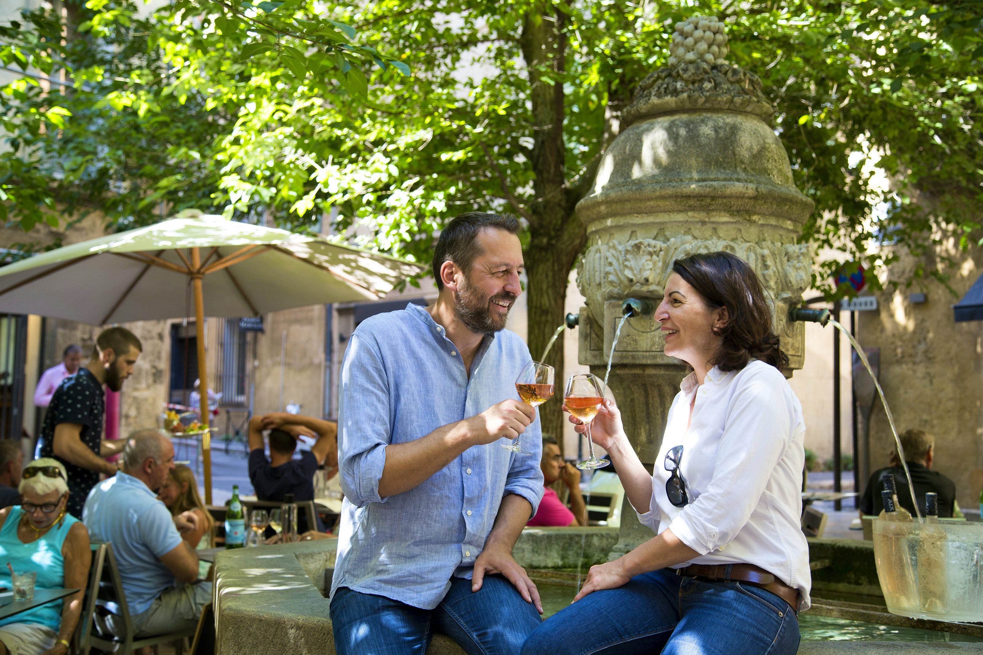 Ein Paar sitzt am Brunnenrand und stösst mit einem Glas Roséwein an